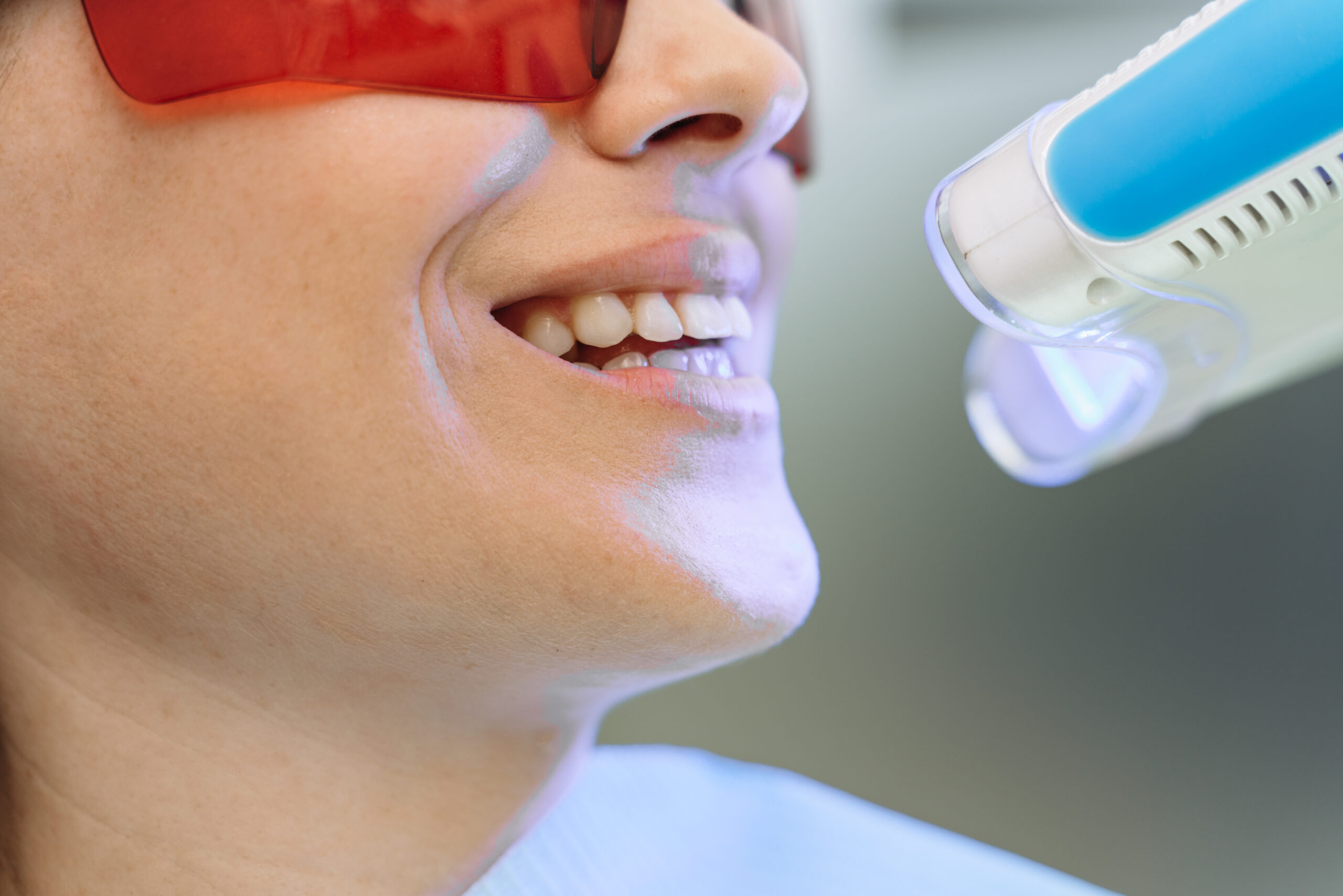 Close up attractive woman in a dental chair with glasses while visiting the dentist. Work equipment shines on the patient's teeth